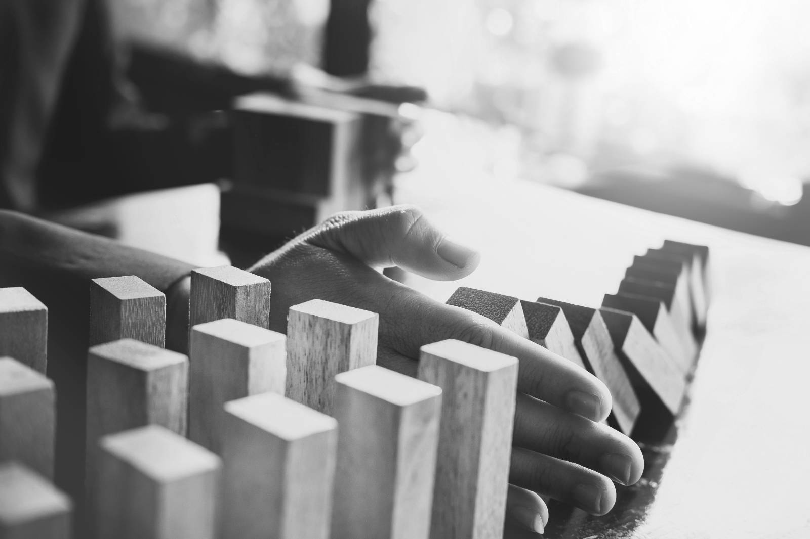 Una mano che ferma una fila di tessere del domino che cadono